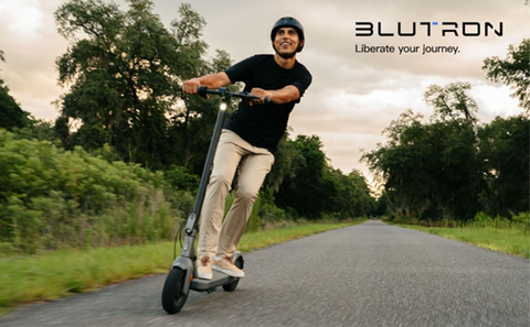 Man joyfully riding a Blutron electric scooter on a scenic road, showcasing speed and freedom.