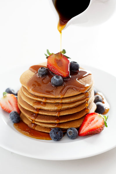 pouring maple syrup over stack of Paleo Pancakes with berries