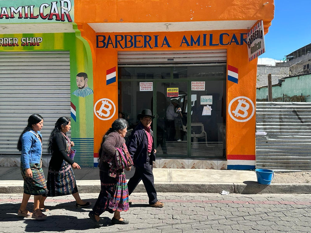 barber shop in guatemala with bitcoin logo painted on the walls and with four people walking in front of it