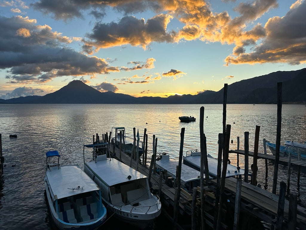 sunset photo of lake atitlan with volcanos in the background, the lake, and boats at the dock