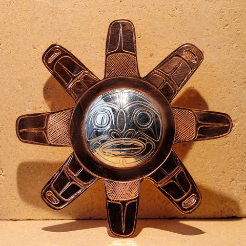 Copper sun pendant with sterling silver face. There are eight rays made of copper coming out from the human-like face.