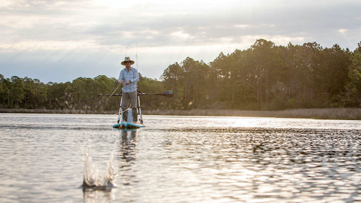 man casting his fishing line while riding on a paddle board