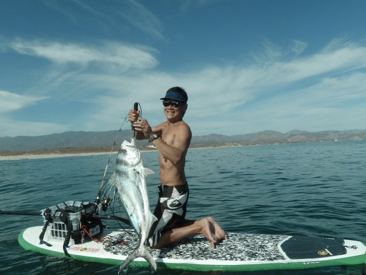 man holding a huge fish over the side of his paddle board