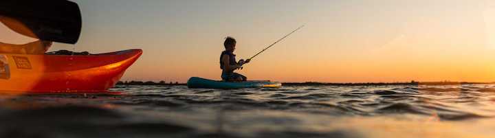 kid fishing off a paddle board at sunset