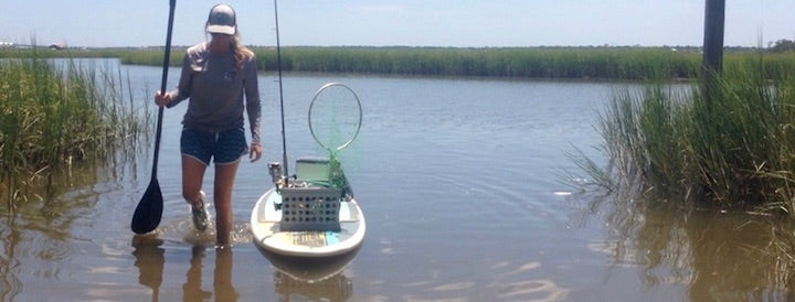 woman wading through water with her paddle board