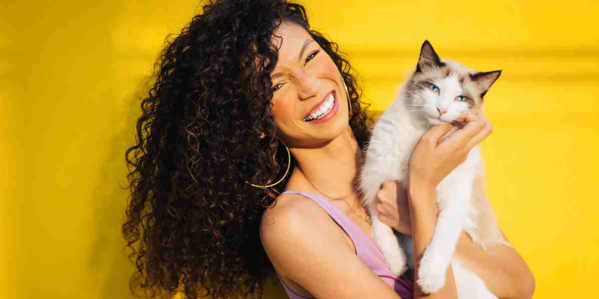 Joyful woman smiling and holding a white Siamese cat, showcasing the bond between pet and owner.