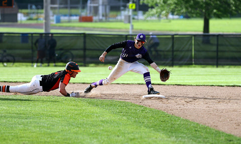 A baseball player fielding a ball while a runner is sliding into the base.