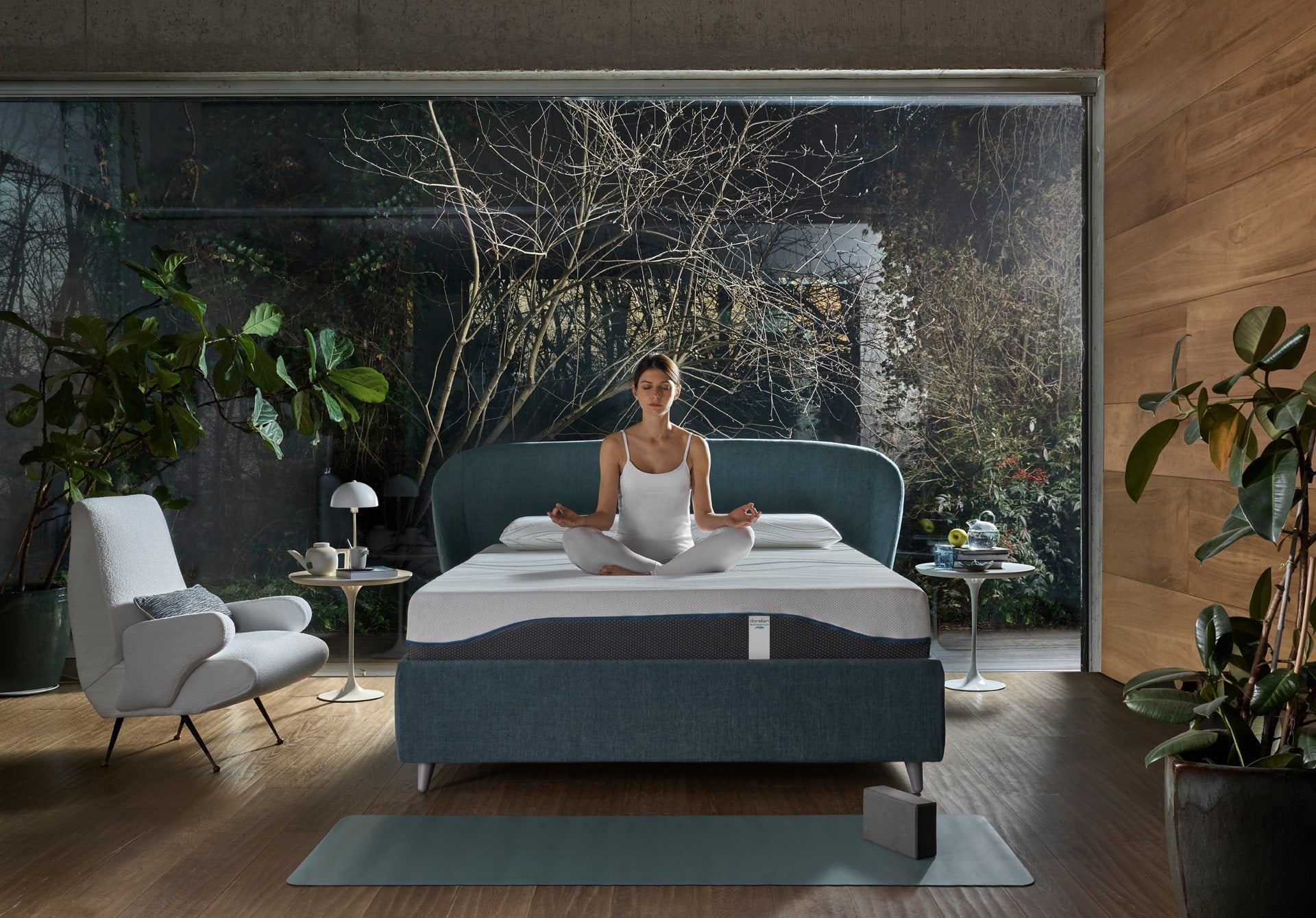 A young woman sits in bed and performs the lotus flower yoga pose.