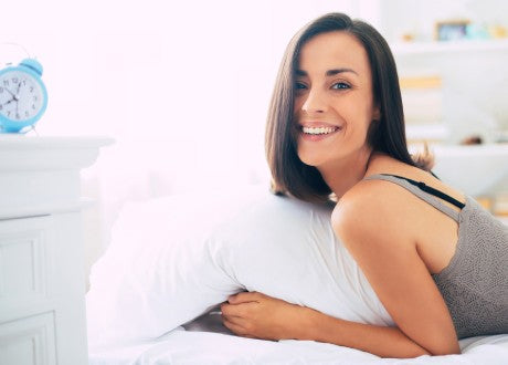 Woman smiling as she lies in bed holding a pillow