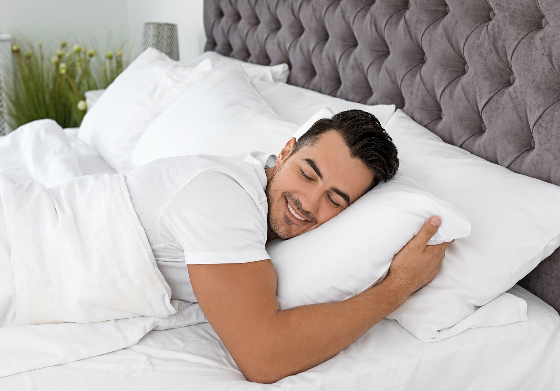 A man resting comfortably in bed, holding a pillow