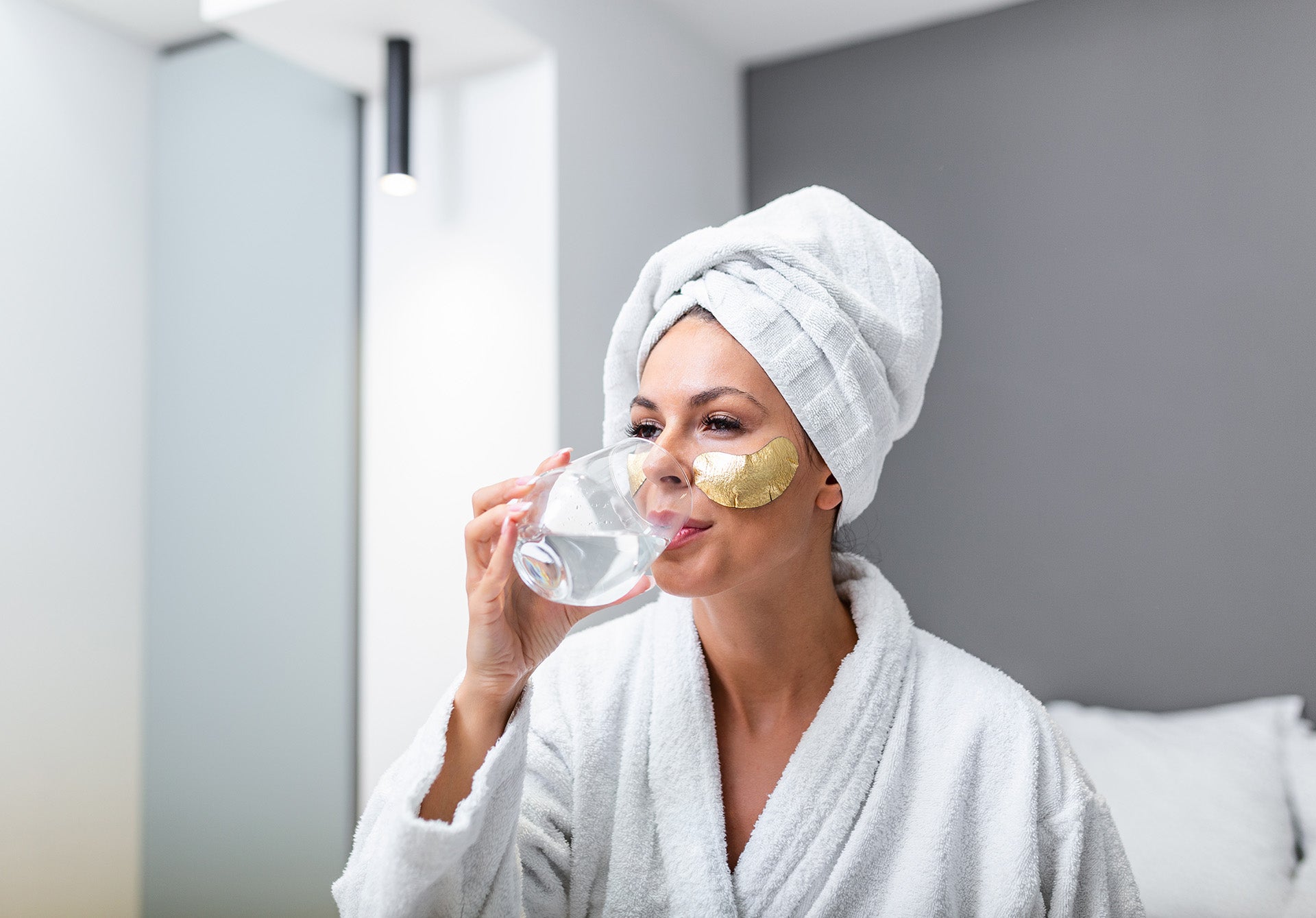 a woman with a towel on her head drinking a glass of water