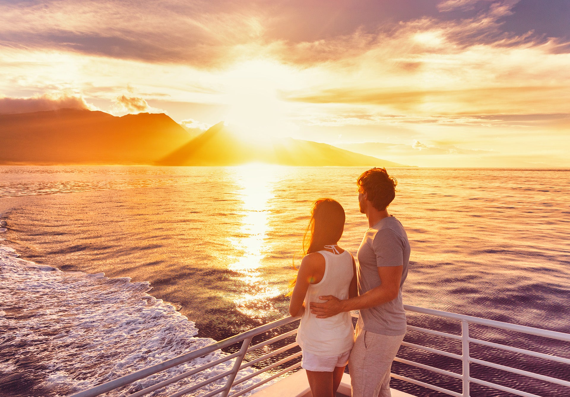 a man and a woman standing on a boat watching the sun go down