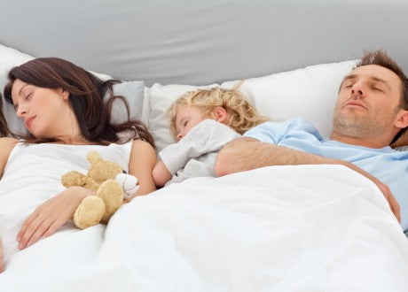 Man, woman, and child sleeping together in a bed with white sheets