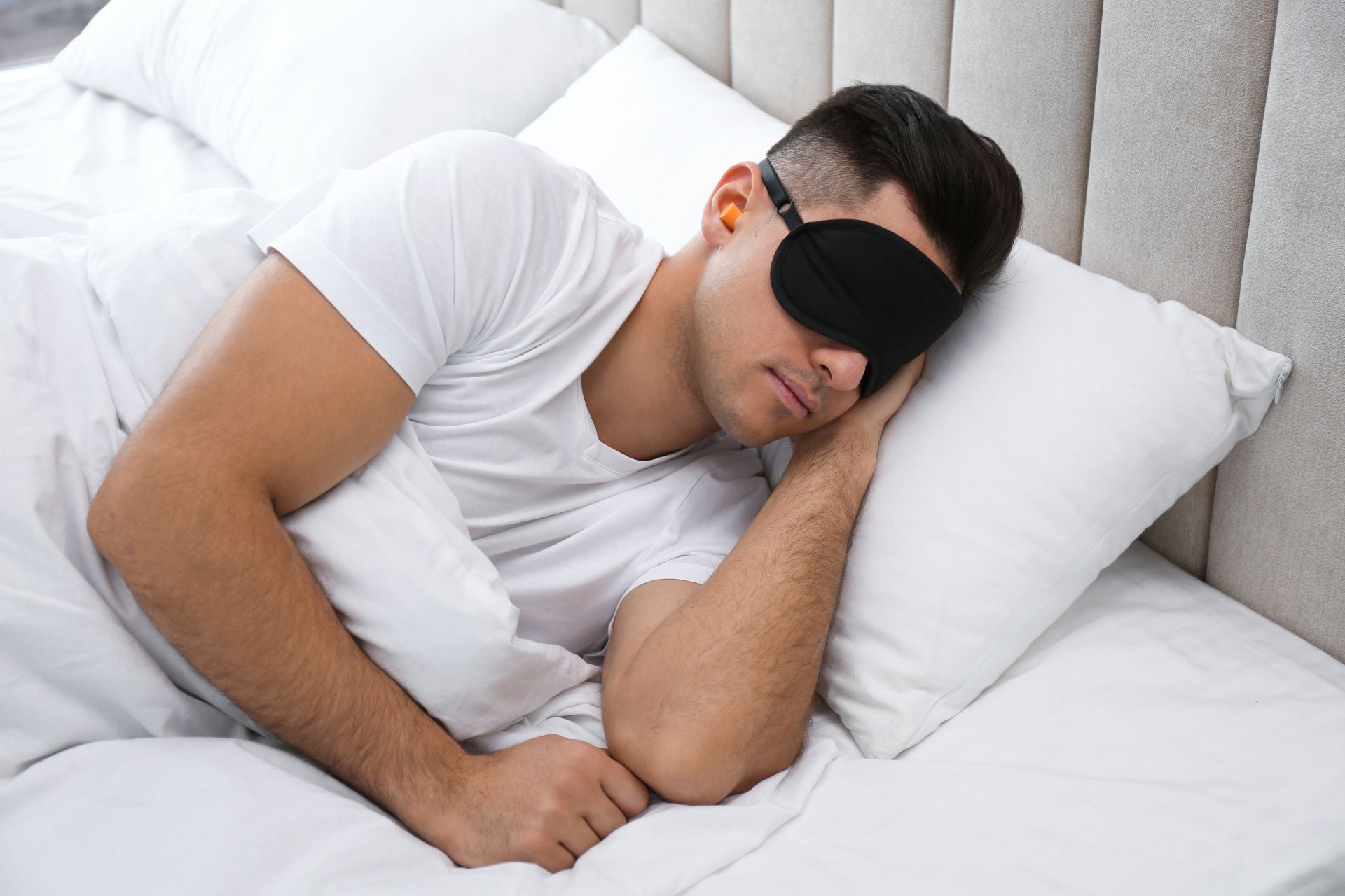 Man wearing sleeping mask and ear plugs in bed