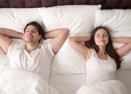 man and woman lying on bed with arms behind their head
