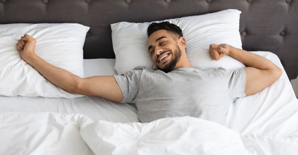 man lying in bed stretching his arms
