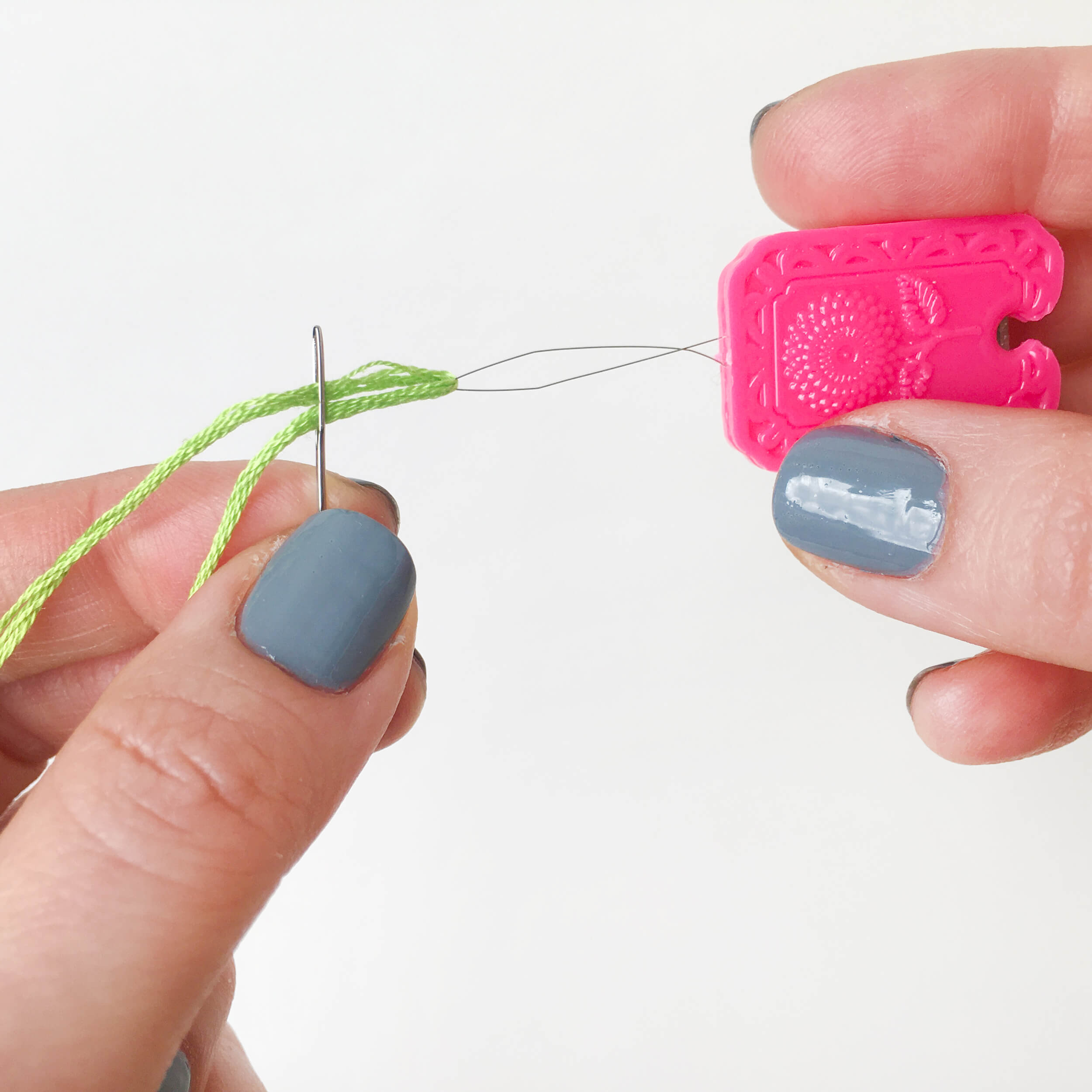 Pink needle threader pulling a grean thread through the eye of a needle