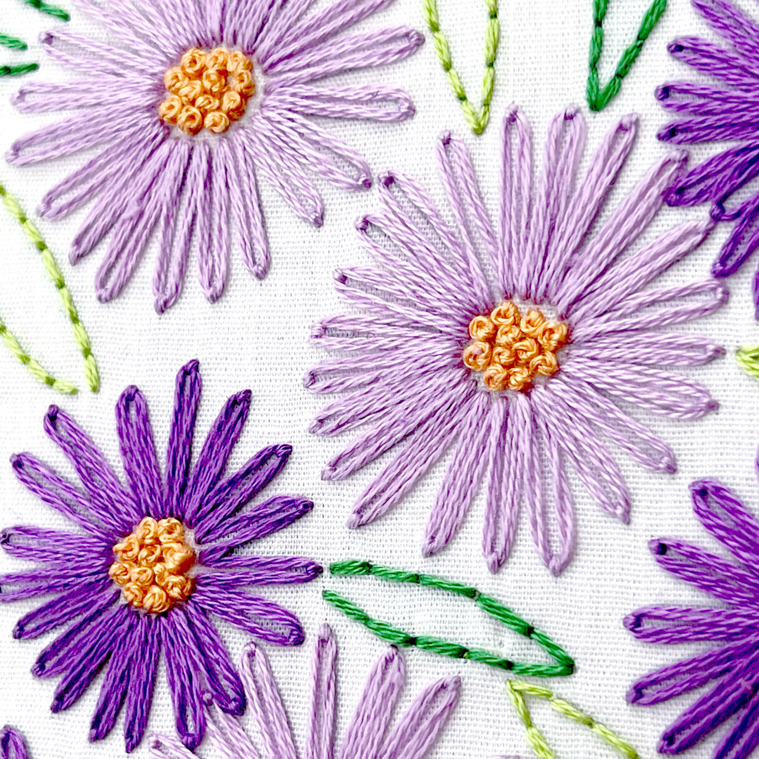 Close up of Aster embroidery flowers with lazy daisy stitch in dark and light purple embroidery floss and orange french knots in the center