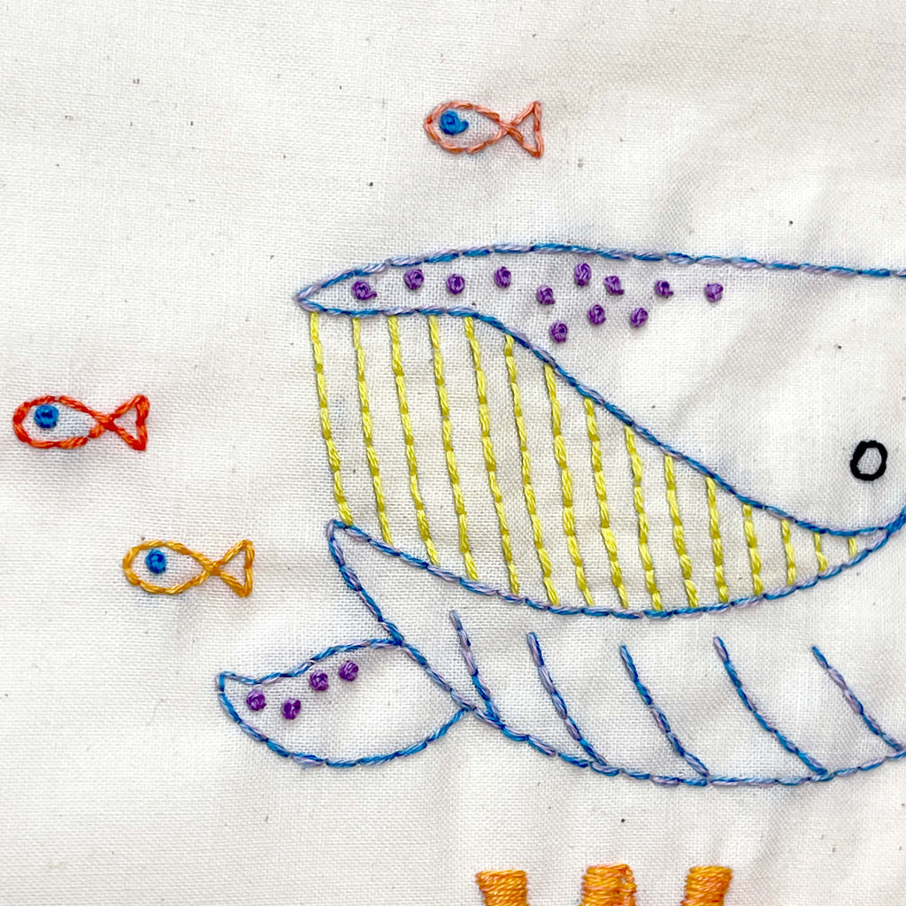 Close up of embroidered whale with small fish swimming next to it.