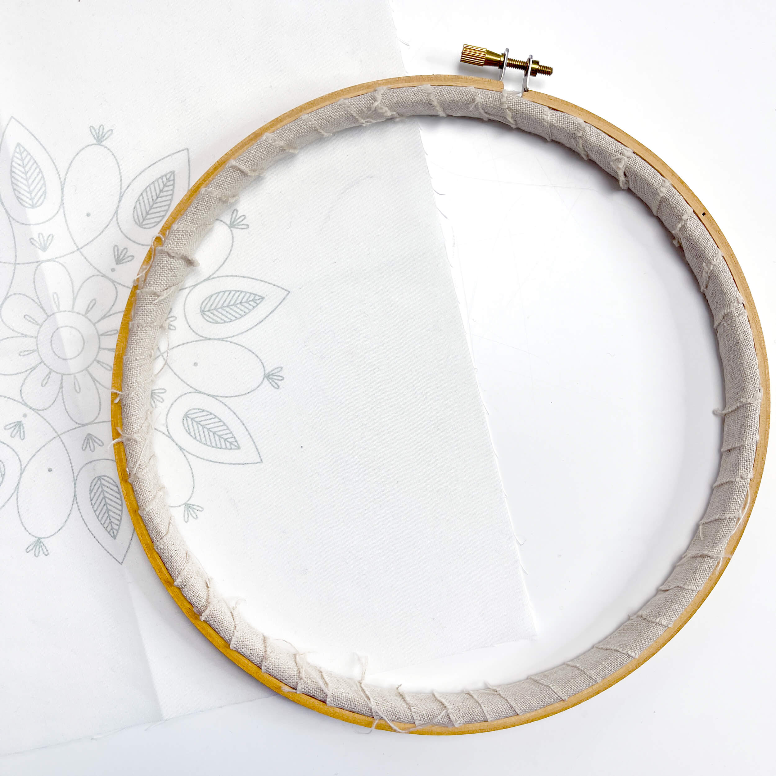Embroidery hoop with fabric wrapped around the inner hoop on top of a fabric pattern
