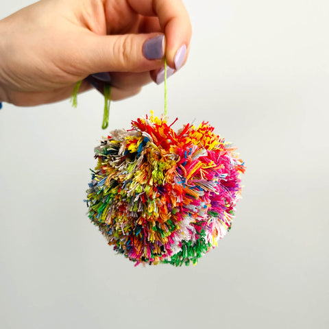 Hand holding an embroidery floss pom pom in a bunch of colors