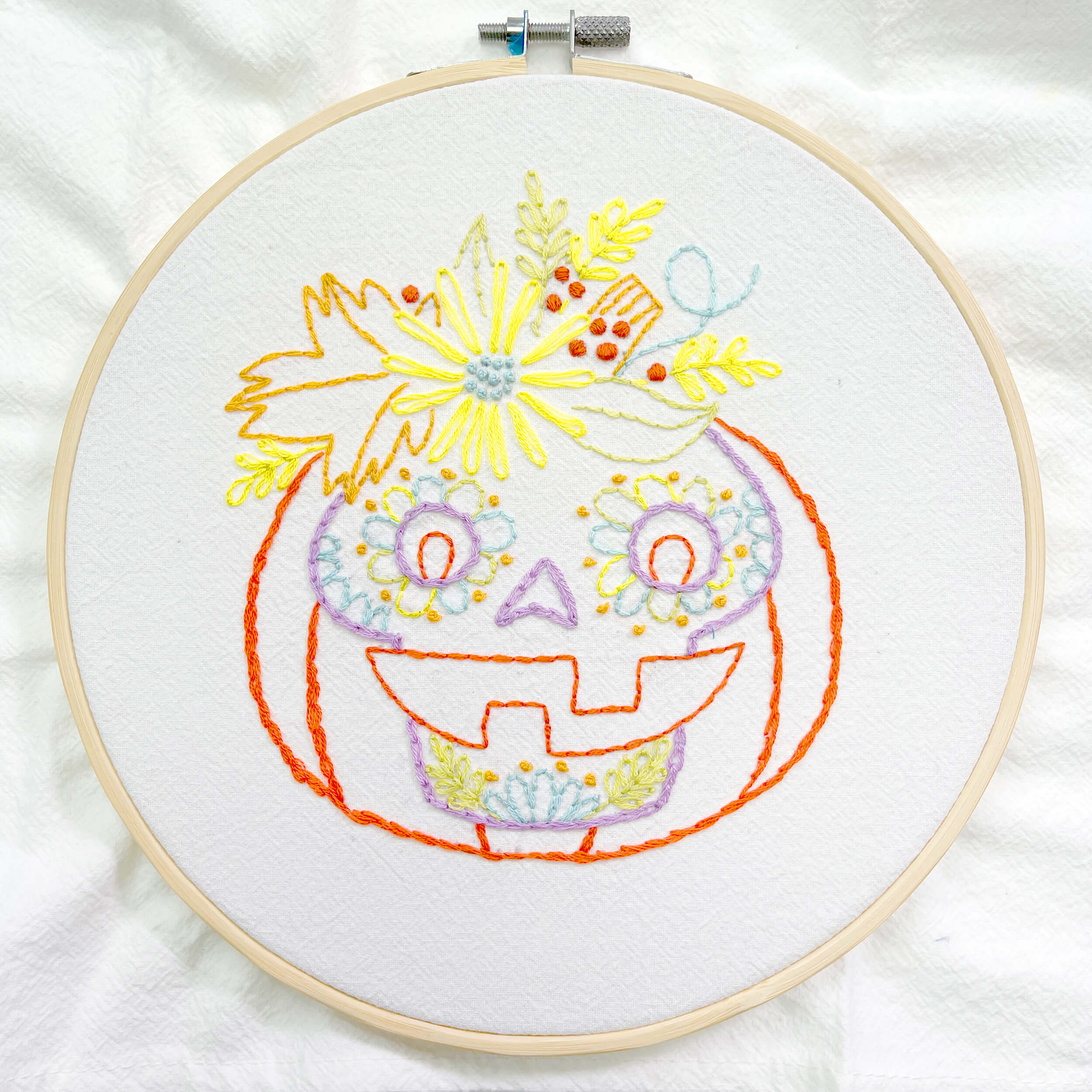 Finished pumpking embroidery with sugar skull face framed in a hoop