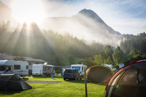 Campsite on a meadow in front of a mountain backdrop with several mobile homes