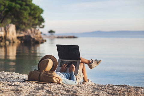 Kvinde ligger på stranden med laptop og arbejder