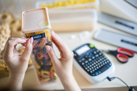 Woman's hands sticking a printed label with the word "pasta" on a transparent box with pasta.