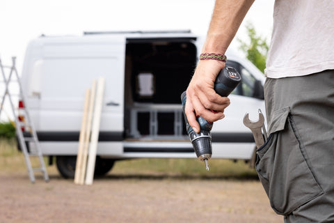 Man with a drill walks towards a van to convert it