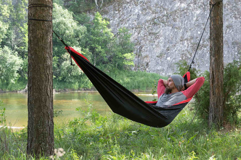 Homem relaxando em uma rede na margem do rio entre duas árvores. 