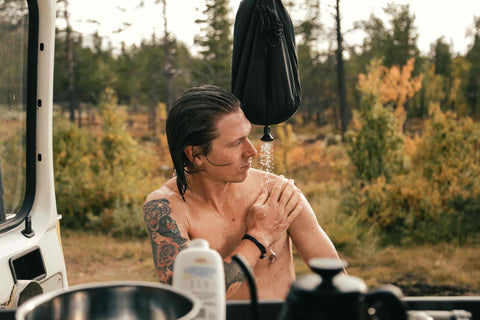 Mann duscht am Camper mit einer Taschendusche im Freien. 