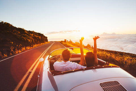 Lykkeligt par i en cabriolet kører ind i solnedgangen