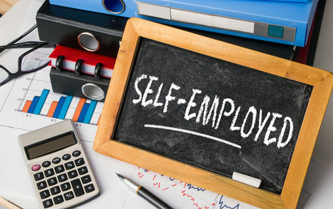Schultafel mit der Aufschrift "Self-Employed" lehnt an Ordnern