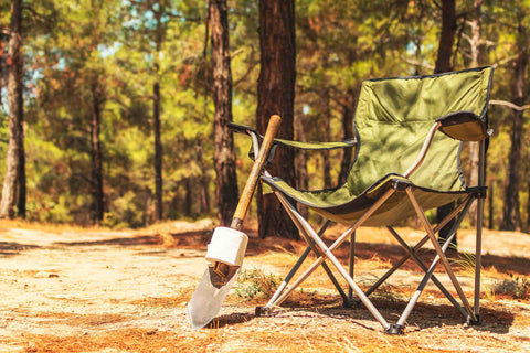 Scene in the forest, foldable camping chair with a shovel leaning against it and toilet paper