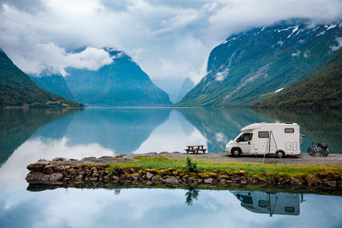 Motorhome is parked on a green strip directly at a mountain lake
