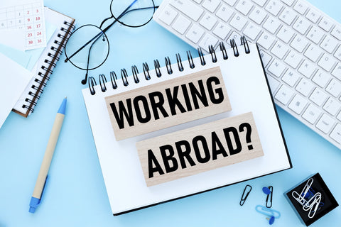 Notesblok med ordene "Working Abroad?" ved siden af kuglepen og tastatur