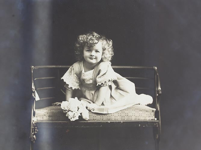 Old fashioned picture of a baby sitting on a bench.