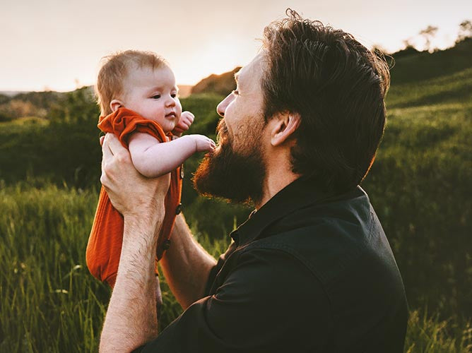Father holding a brand new infant outdoors in a green, earthy backdrop.