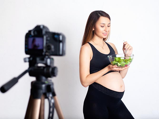 Famous, pregnant influencer doing a photoshoot while eating salad.