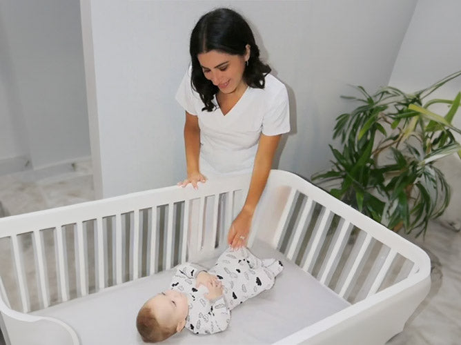 Nicole Morales standing over a crib looking at a baby.
