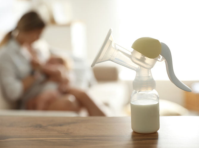 Closeup of a breast pump attachment with a mother feeding in the background.