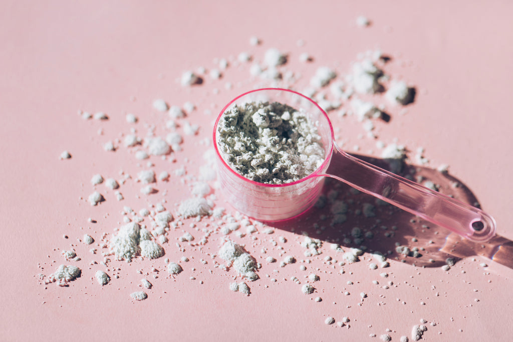 Measuring spoon with collagen powder or alginate mask on a pink background.    