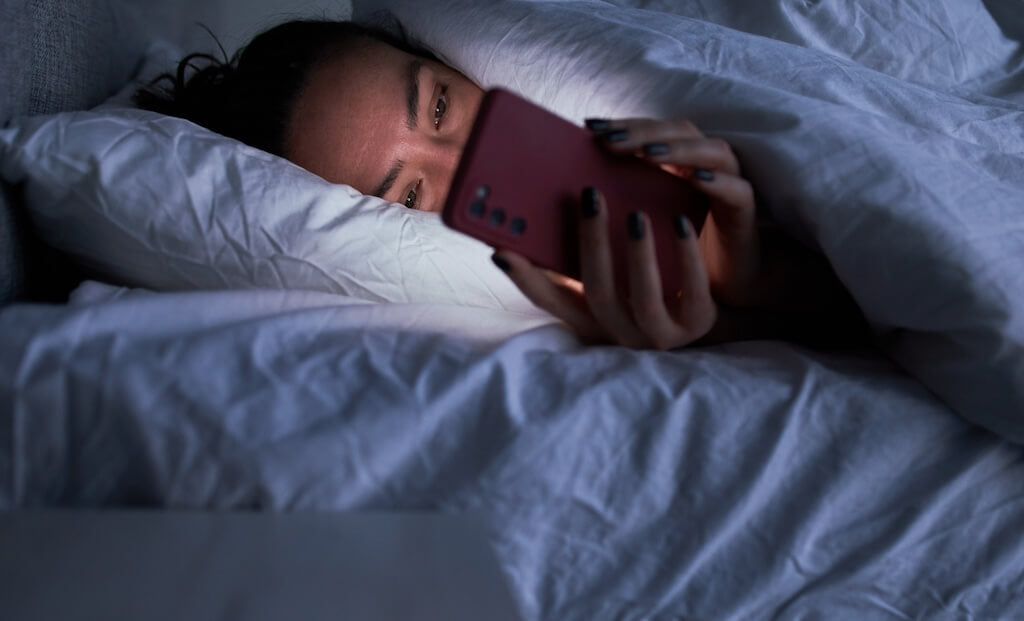 woman looking at her phone in bed at night