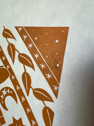 A corner of an orange lino print showing a small black mark
