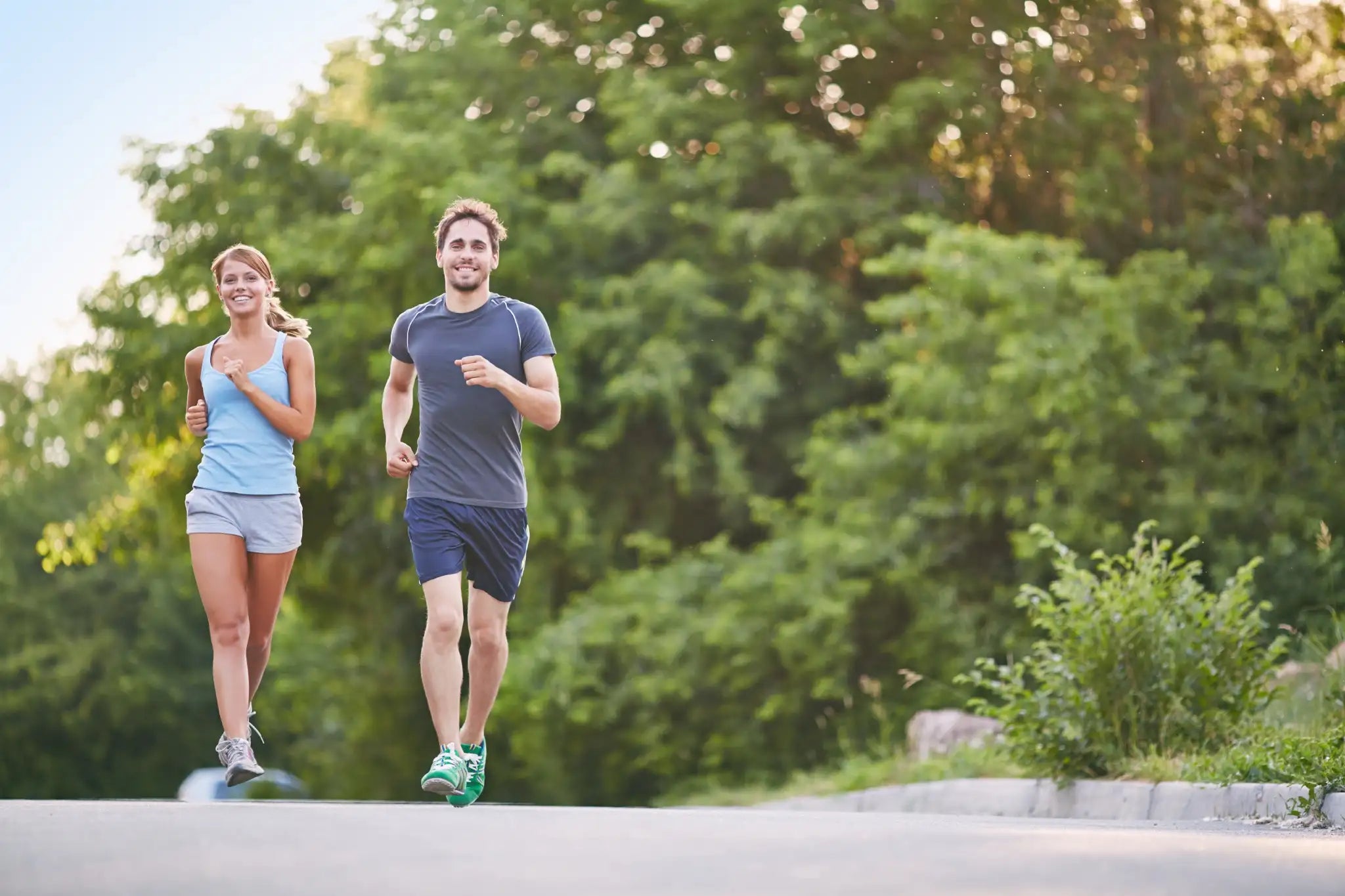 Couple enjoying their first run back after half marathon recovery, jogging on a tree-lined path.
