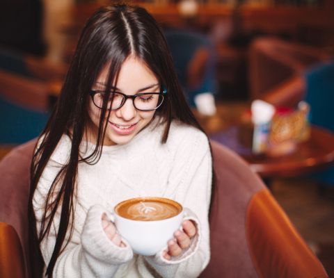 jeune femme qui sourie tout en regardant son excellent café
