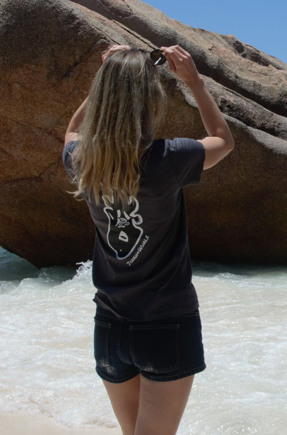 girl wearing a shirt with a whale logo on back stands at the seaside