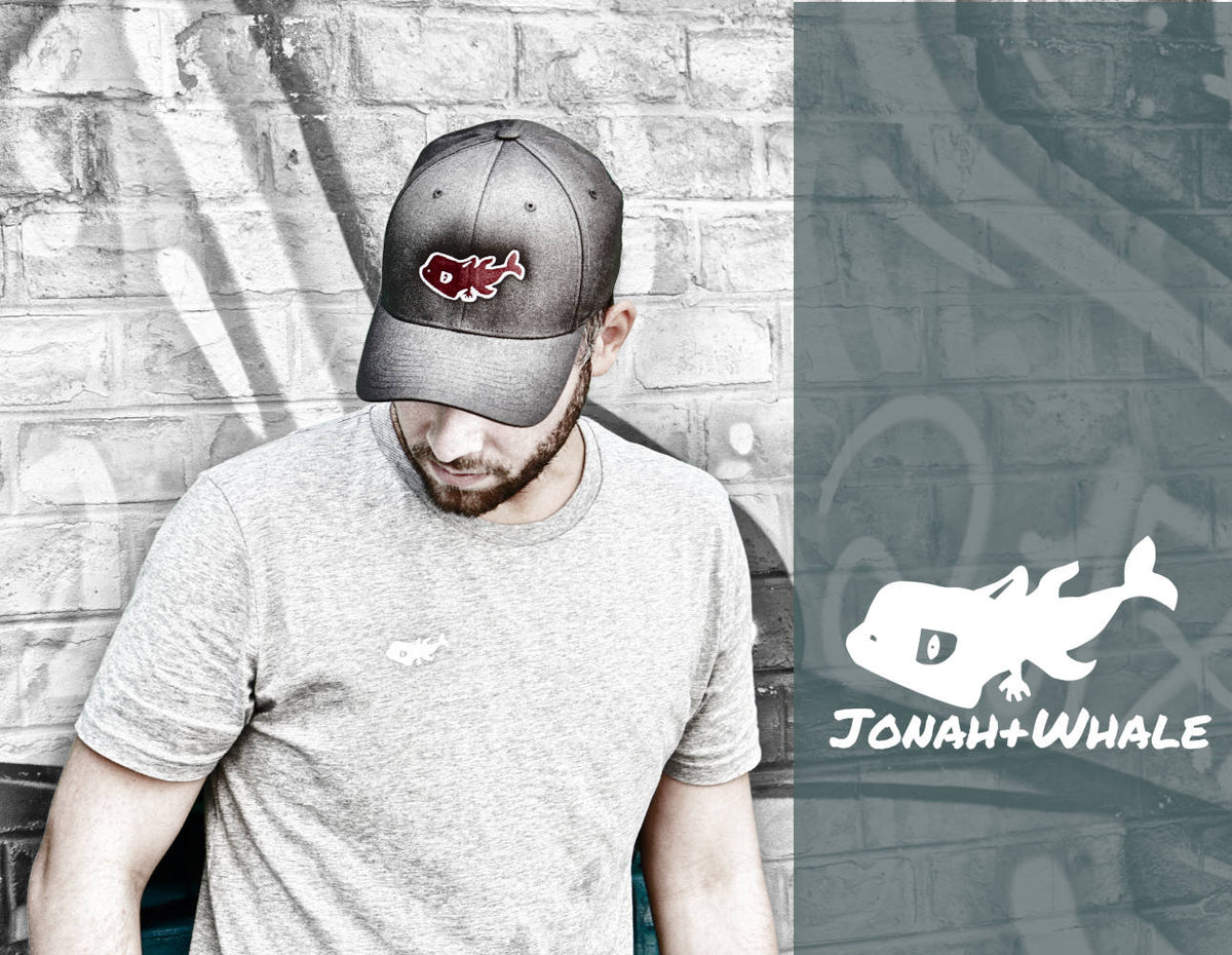 man wearing a cap with a red whale logo stands in front of a brick wall which is partly covered with a green overlay and a white whale logo