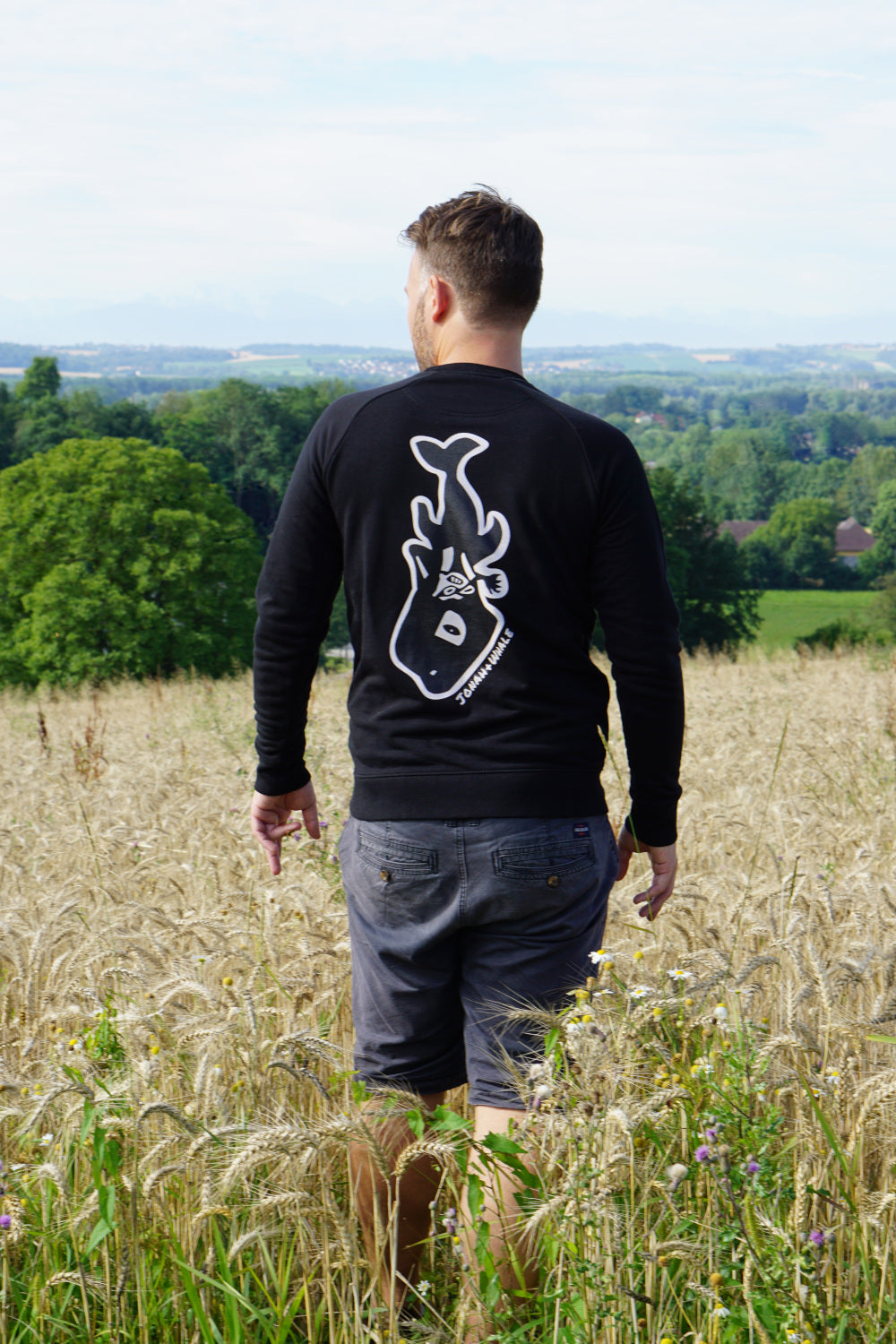 man wearing a sweatshirt with a whale logo on back stands in the field